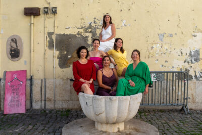 Bachelorette photoshoot in Lisbon, group of friends in colorful dresses sitting in a stone fountain